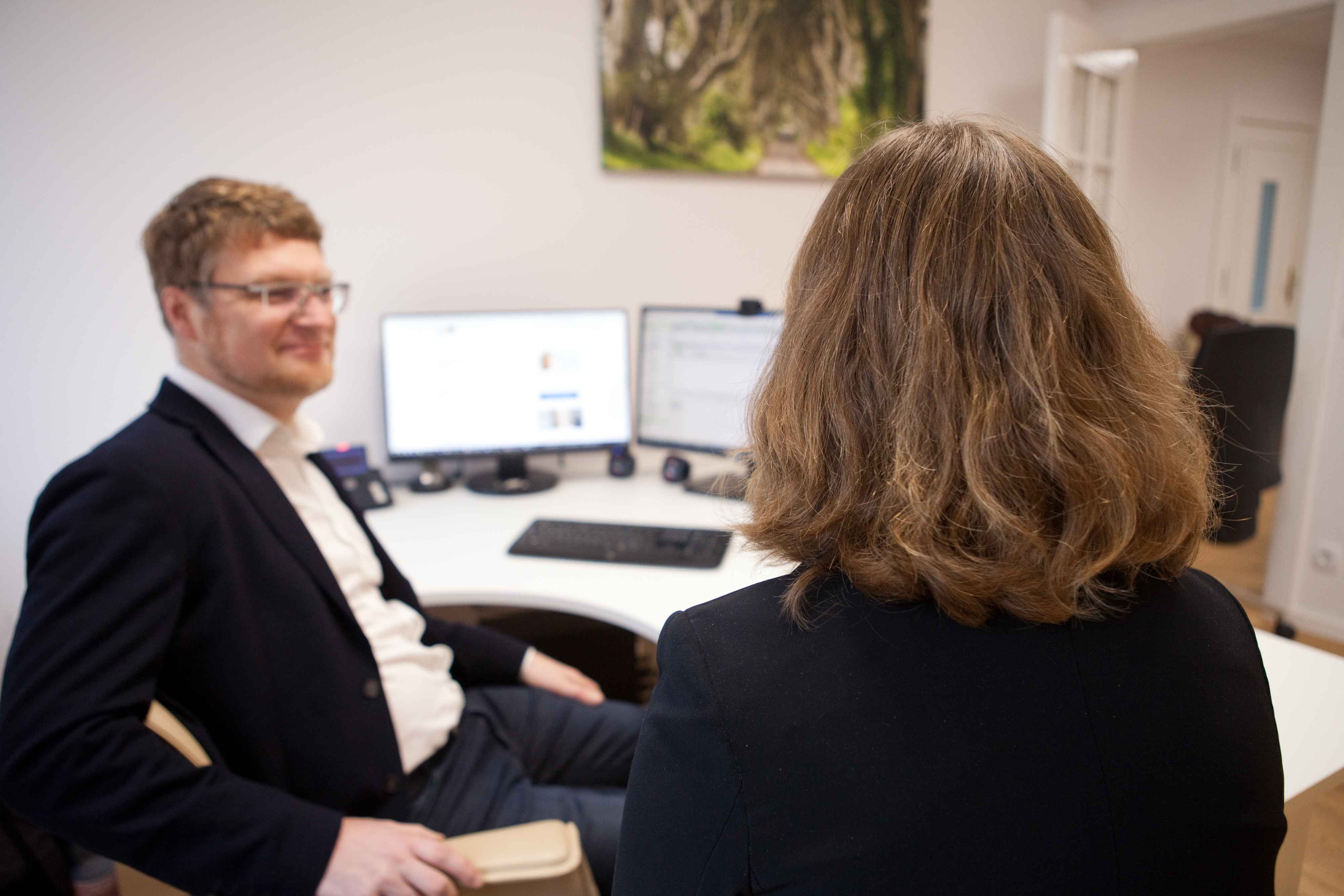 Zwei Personen im Gespräch am Tisch, Rückenansicht, Mann frontal – Teambesprechung.