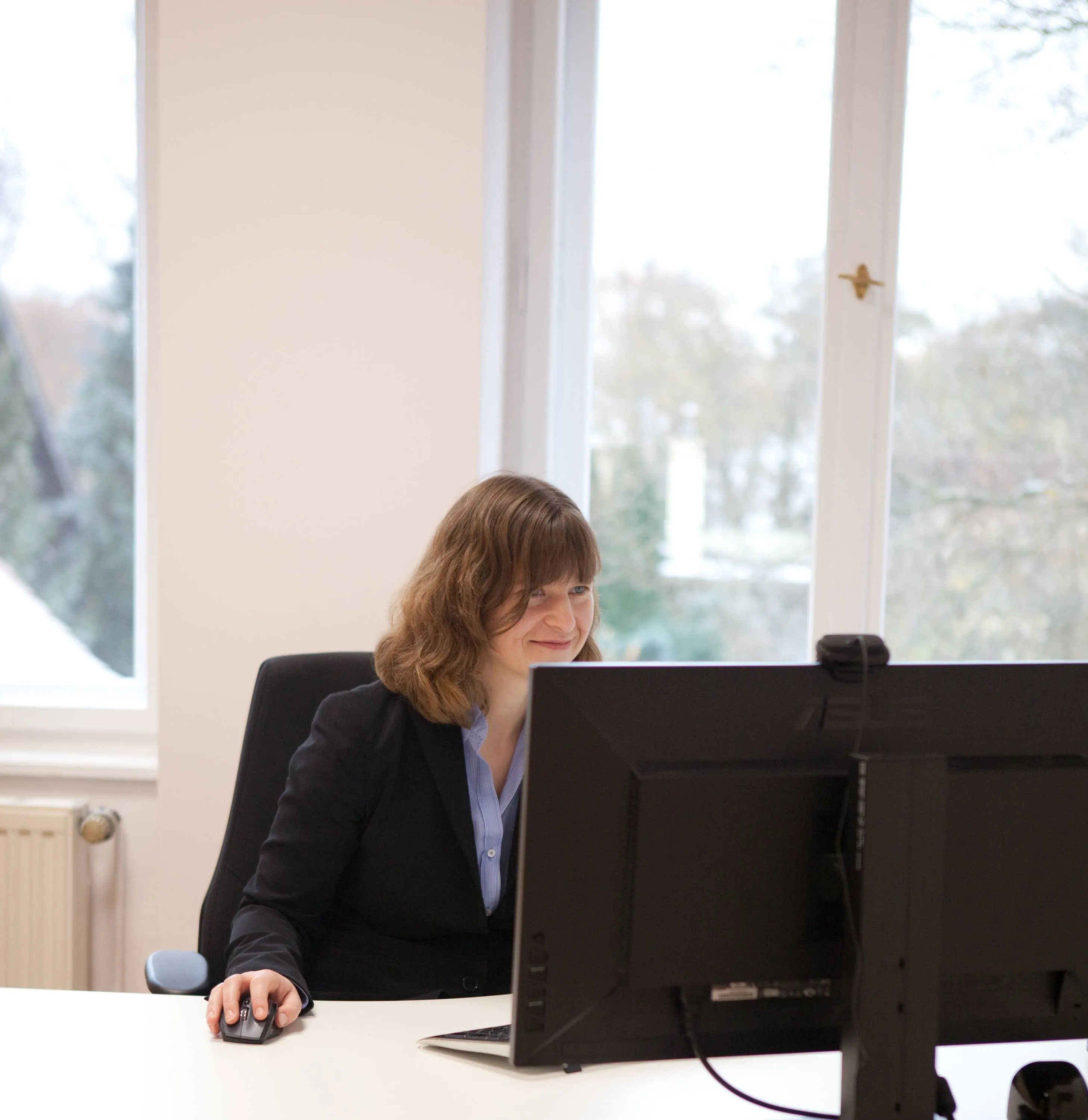 Frau arbeitet am Schreibtisch mit Computer, Fenster im Hintergrund – Arbeitsplatz.