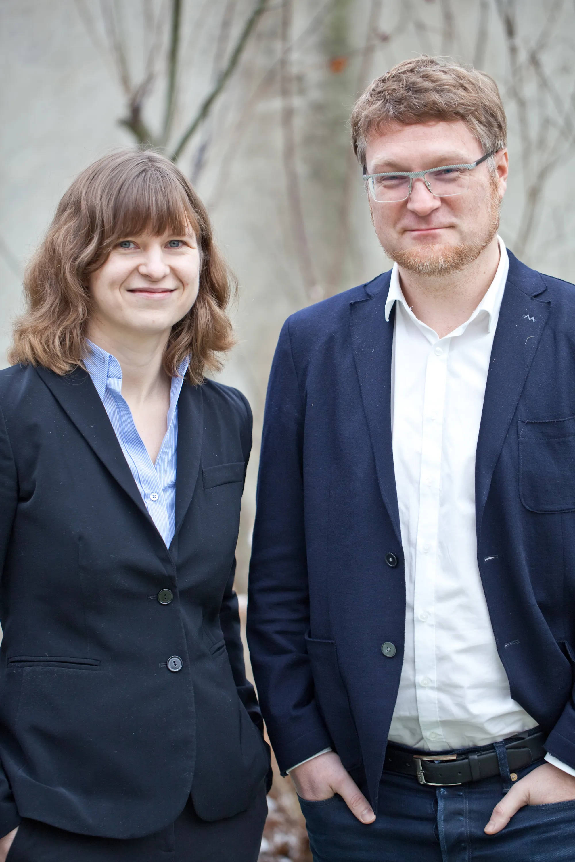 Mann und Frau im Business-Outfit draußen, lächeln in die Kamera – Teamfoto außen.