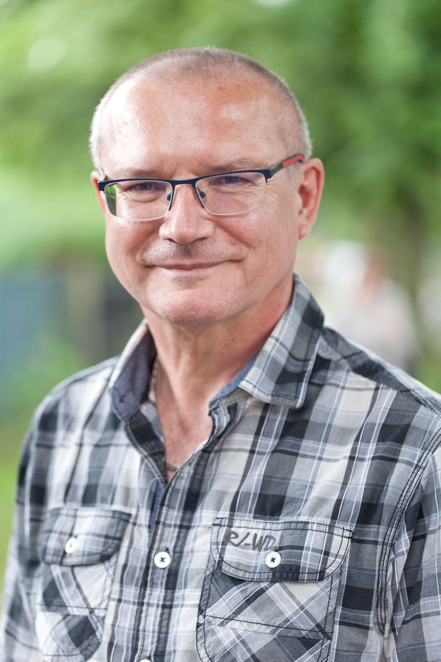 Porträt eines älteren Mannes mit Brille, freundlicher Blick, grüner Hintergrund