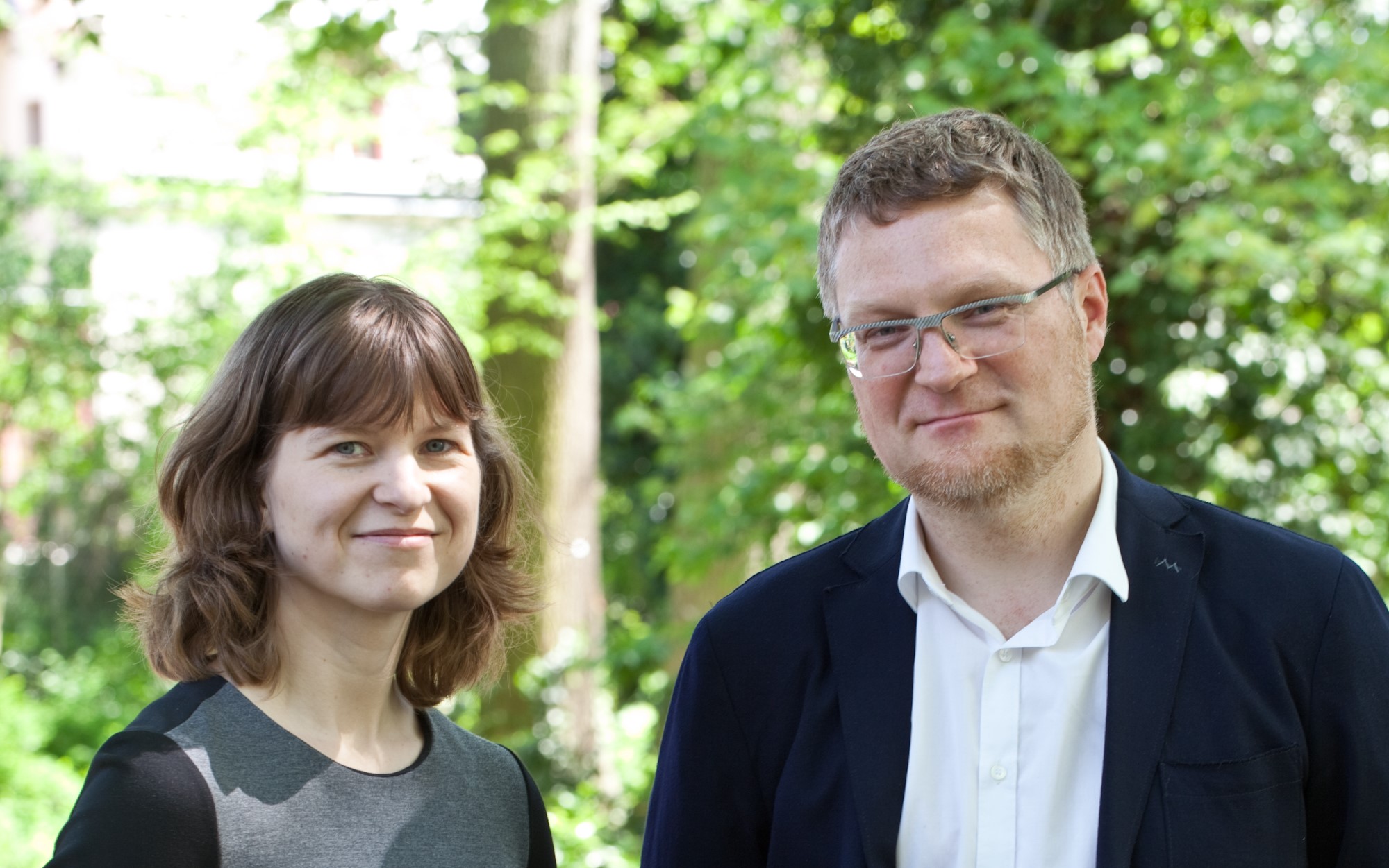 Mann und Frau lächeln in die Kamera, Bäume im Hintergrund – Teamfoto.