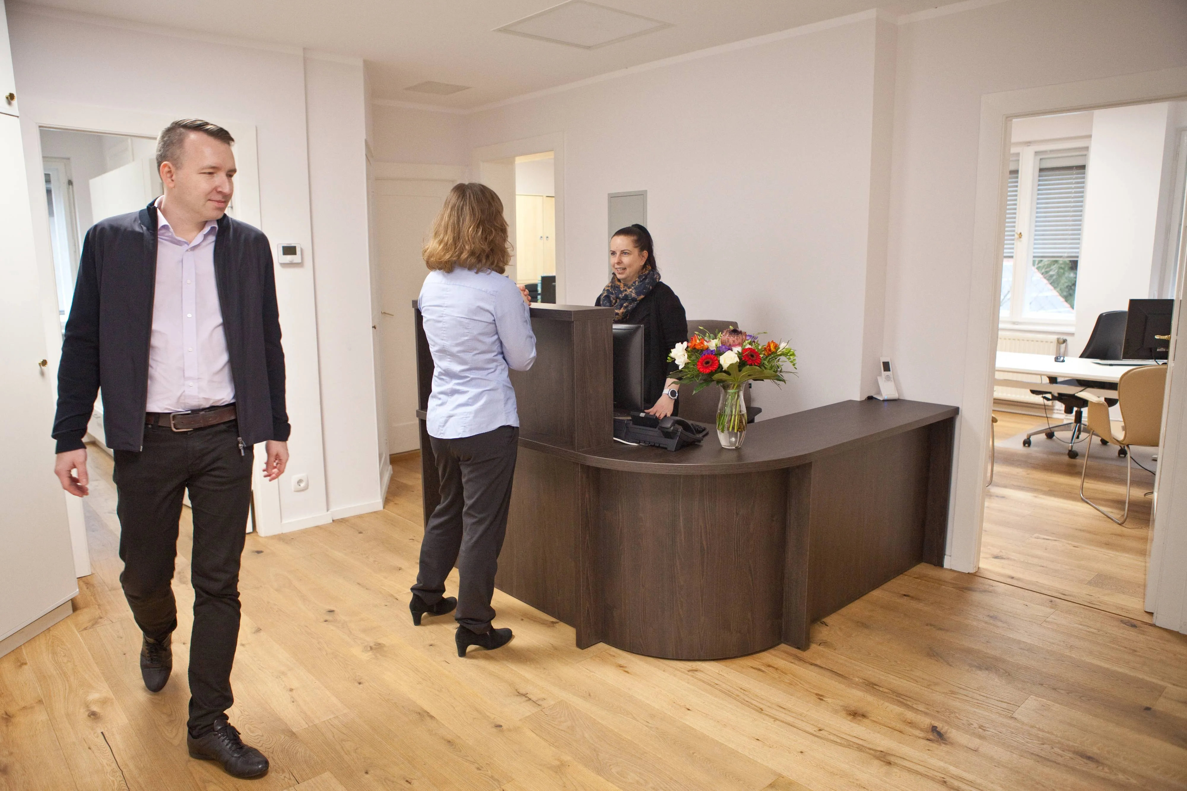 Mann geht durch Flur, Frau am Empfang – Alltag im Büro.