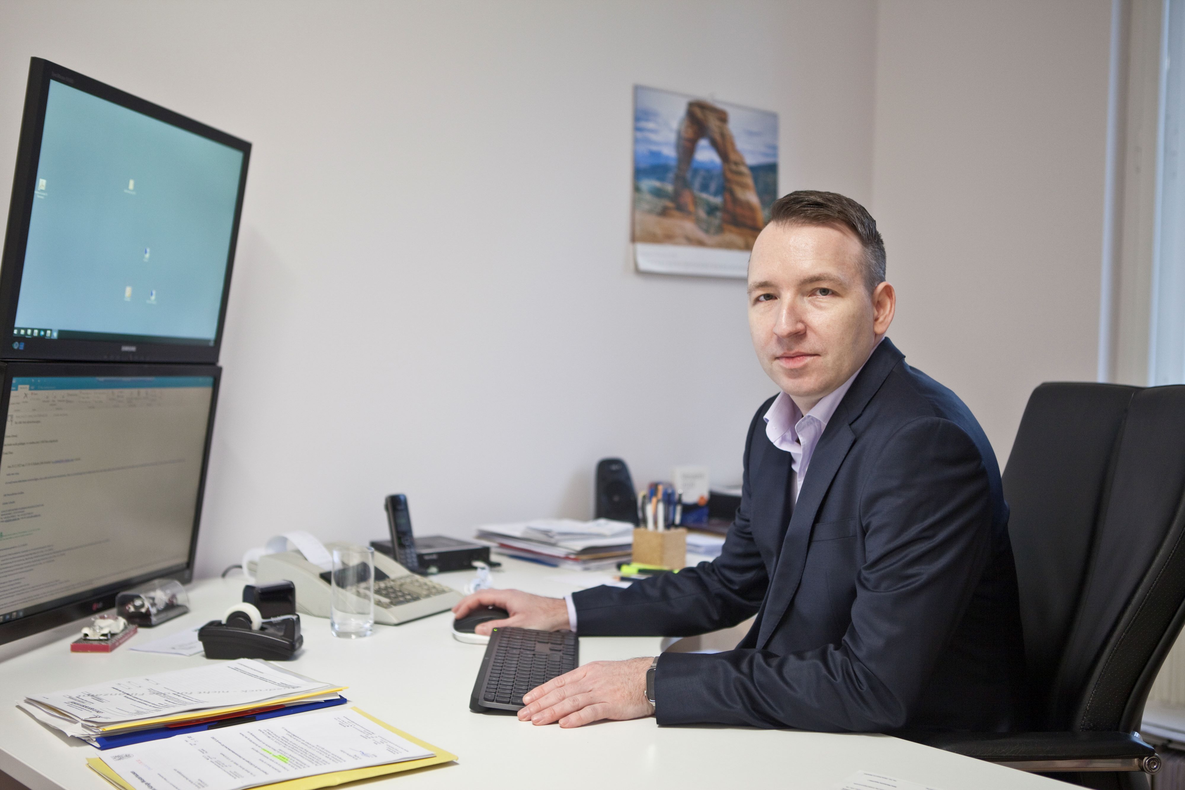Mann im Anzug am Schreibtisch mit Computer, schaut zur Kamera – Arbeitsplatz.
