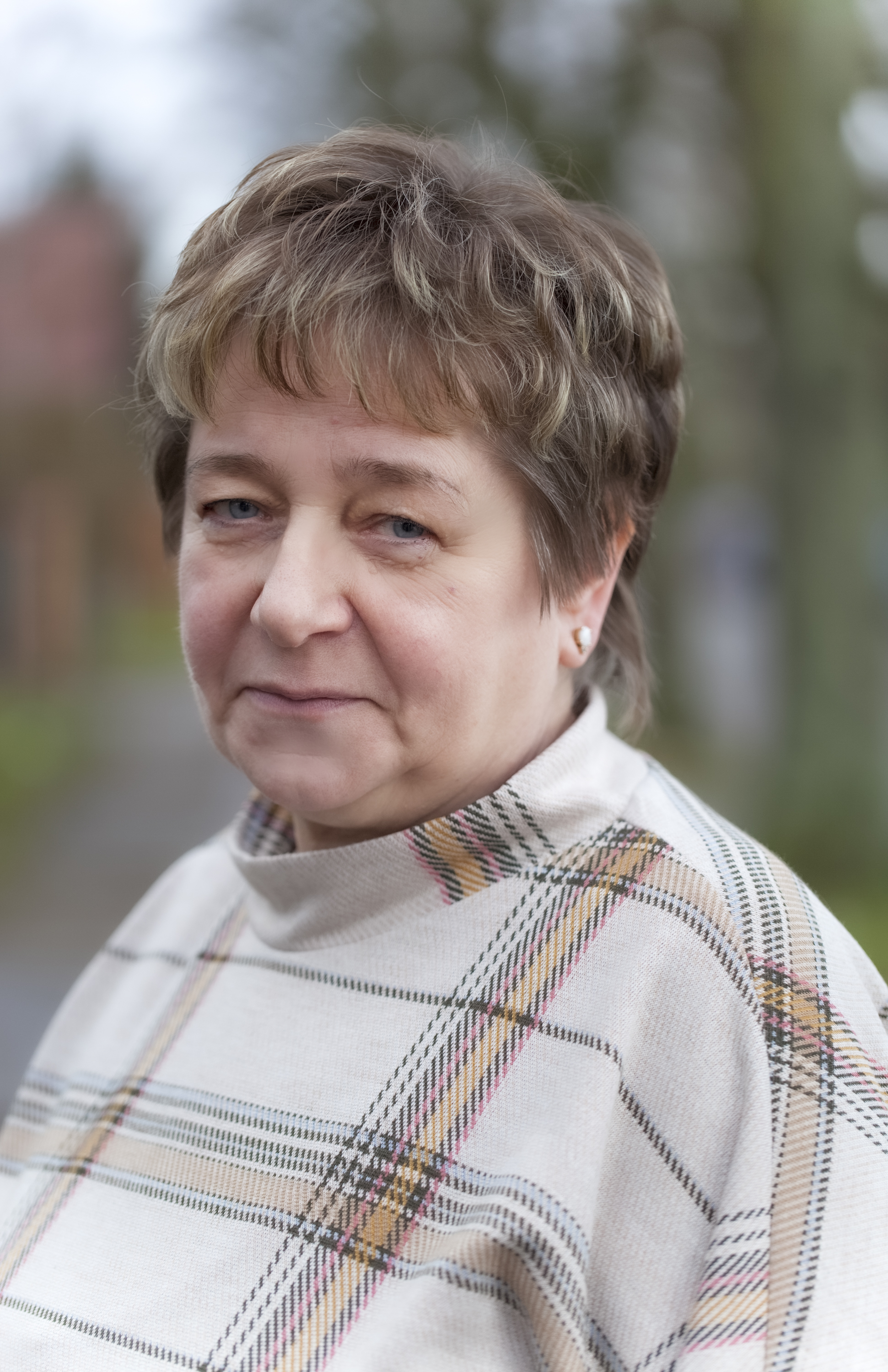 Porträt einer Frau mit Kurzhaarfrisur, kariertes Oberteil, Bäume im Hintergrund – Mitarbeiterin.