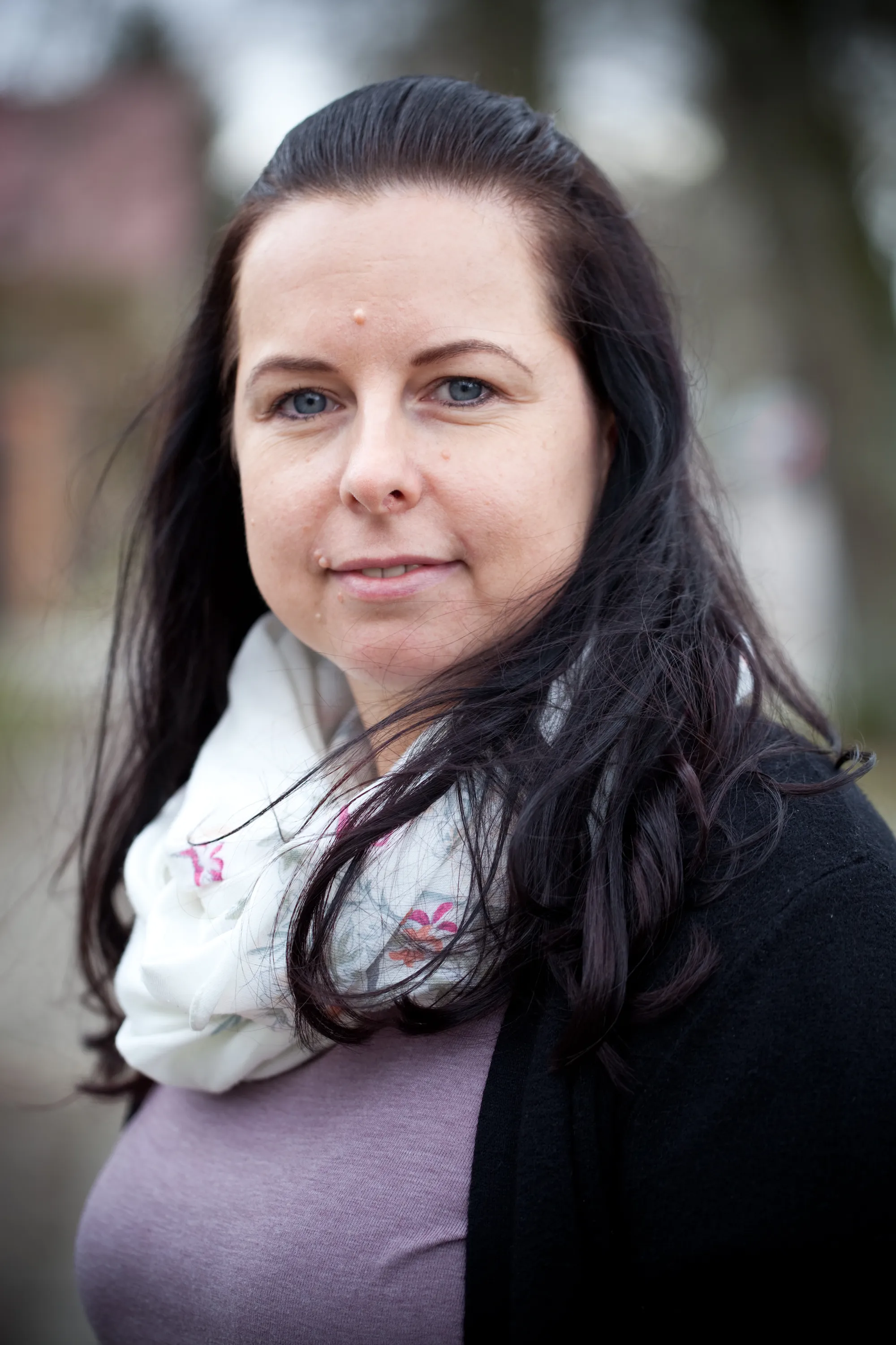 Porträt einer Frau mit dunklen Haaren, Schal, Natur im Hintergrund – Teamfoto.